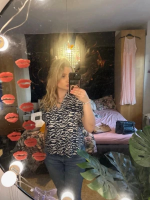 Mönstrad blus i blått och vitt - Snygg blus med blå och vitt abstrakt mönster. Blusen har korta ärmar och en avslappnad passform med v-ringning. Perfekt att matcha med jeans för en trendig look. Materialet ser ut att vara mjukt och lätt, troligen viskos eller bomull.