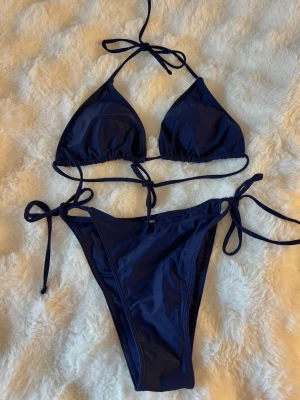 Mörkblå trekantsbikini med knyt - Snygg mörkblå bikini med trekantsmodell och knyt i både topp och trosa. Klassisk och enkel design som passar perfekt till stranden eller poolen. Tillverkad i mjukt och stretchigt material för skön passform.