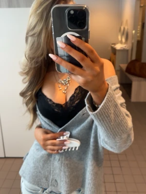 Svart spetsbody med tunna axelband - Säljer en svart body med tunna axelband och vacker spetsdetalj längs urringningen. Bodyn har en figurnära passform och ger en snygg siluett. Perfekt att styla under en kofta eller till jeans för en trendig look.