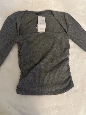 Grå ribbad långärmad topp - Snygg grå ribbad topp med lång ärm och figurnära passform. Toppen har en enkel, stilren design och är tillverkad i ett mjukt material som passar perfekt till olika outfits. Perfekt för dig som gillar en clean och modern look.