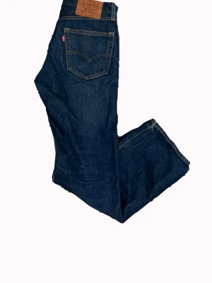 Mörkblå raka jeans från Levi's - Klassiska mörkblå jeans från Levi's med rak passform och fem fickor. Jeansen har en ikonisk läderpatch bak i midjan och röd Levi's-tag på bakfickan. Tillverkade i slitstark denim med snygga kontrastsömmar. Storlek 28/30