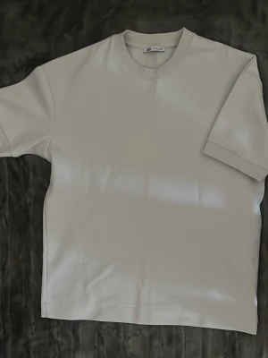Vit t-shirt från Zara - En stilren vit t-shirt från Zara med klassisk rund halsringning och korta ärmar. T-shirten är tillverkad i mjuk bomull och har en enkel, clean look som passar till det mesta. Perfekt basplagg för garderoben.