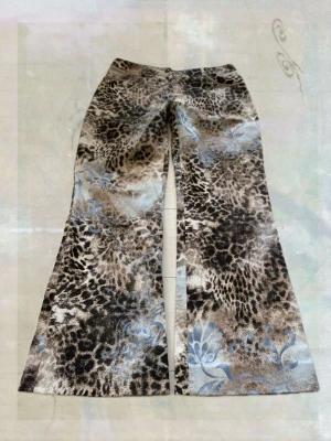 Bruna utsvängda jeans med mönster - Säljer ett par bruna utsvängda jeans med leopardliknande mönster och ljusblå blommor. Jeansen har hög midja och vida ben, vilket ger en retrovibe. Perfekta för dig som vill sticka ut med ett unikt plagg i garderoben. 70 cm innerbenslängd , 80cm midja 