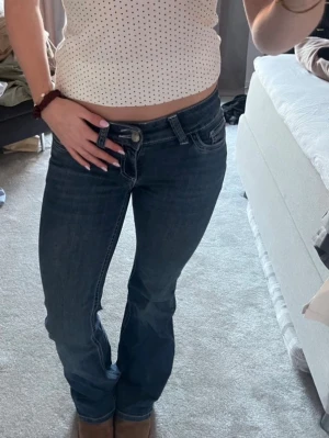 Mörkblå bootcut jeans  - Säljer ett par mörkblå bootcut jeans med vita kontrastsömmar och klassiska fem fickor. Jeansen har låg midja och detaljerade bakfickor. Perfekta för en avslappnad och trendig look. 