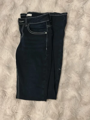 Jeans från Gina tricot  - För bilder på så kom privat 😊Mörkblå jeans från Gina tricot  med vita kontrastsömmar och snygga fickdetaljer med lock och knapp bak. Klassisk femficksmodell med normal passform och raka ben. Perfekta för dig som gillar en stilren men ändå unik look.