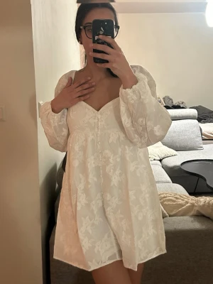 Vit klänning från GinaTricot - Supersöt vit klänning med blommigt mönster och puffiga långärmar. Klänningen har v-ringning och en luftig passform som gör den både fin och bekväm samtidigt. Den är aldrig använd då jag råkade beställa två st. Den är från GinaTricot och nypris är 600kr.