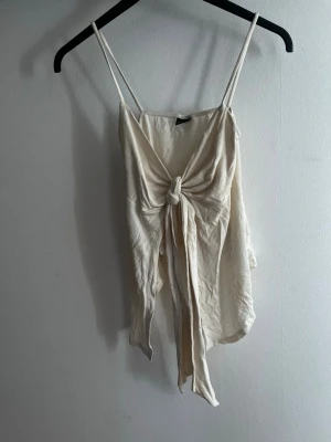 Krämvit linnetopp med knyt från Gina Tricot - Säljer en krämvit linnetopp från Gina Tricot med tunna axelband och snygg knytning framtill. Toppen har en luftig och lätt känsla, perfekt för varma dagar. Enkel att styla med både jeans och kjol. Aldrig använd