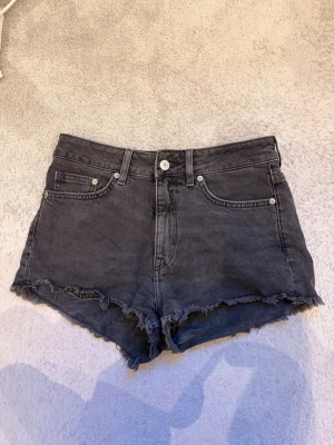 Svarta högmidjade jeansshorts - Säljer ett par svarta  jeansshorts. Shortsen har knapp och dragkedja framtill samt bälteshällor. Shortsen är ifrån H&M och är i storlek EUR 36