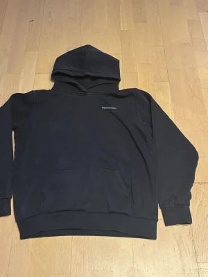 Peak Performance Hoodie - Säljer en mörkblå hoodie från Peak Performance med broderad logga på bröstet. Klassisk känguruficka framtill och ribbade muddar vid ärmar och nederkant. Tillverkad i mjukt bomullsmaterial och har en stor huva för extra komfort.