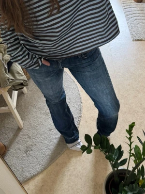 Blå lågmidjade raka jeans från Levi's - Säljer ett par klassiska blå jeans från Levi's med raka ben och snygga kontrastsömmar. Jeansen har fem fickor och en liten röd Levi's-tag bak. Perfekta till en avslappnad stil och passar till det mesta i garderoben.