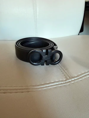 Svart skärp från Salvatore Ferragamo - Snyggt svart skärp från Salvatore Ferragamo med ikoniskt dubbel-Gancio-spänne i matt svart metall. Bältet är gjort i slätt skinn och har en stilren, modern look som passar till många outfits.