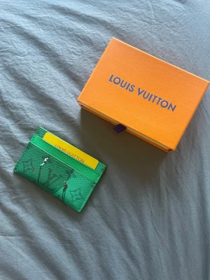 Grön kortfodral - Snyggt grönt kortfodral med klassiskt monogrammönster och diskreta färgdetaljer. Tillverkad i exklusivt läder och har plats för flera kort. Perfekt accessoar för dig som vill ha något unikt och trendigt från ett lyxigt märke.