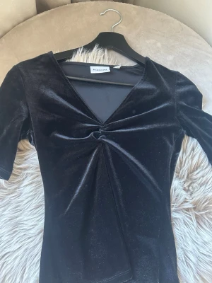 Svart topp - Snygg svart topp i mjuk sammet från Kappahl. Toppen har v-ringning, korta ärmar och en twistad detalj framtill. Perfekt att styla med jeans eller kjol för en trendig outfit.