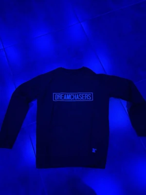 Svart sweatshirt Dreamchasers - Cool svart sweatshirt från Dreamchasers med vit textlogga på bröstet och liten DC-detalj vid nederkanten. Tröjan har rund hals och långa ärmar, perfekt för en avslappnad streetwear-look.