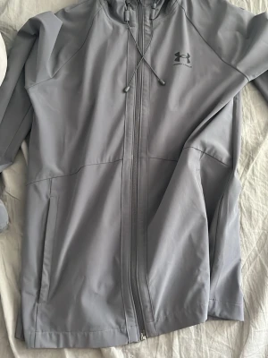 Ljusgrå vindjacka från Under Armour - Säljer en fin vindjacka från underarmour, bara stått i garderoben sen jul, den är använd några gånger men inte mer än så.
