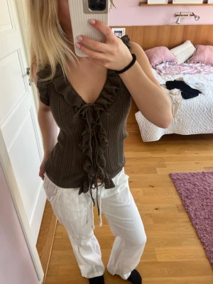 Topp från Zara  - Supersnygg mörkgrön ribbad topp med volangkant längs urringningen och snörning framtill. Toppen har korta ärmar och en v-ringad design som ger en trendig look. Perfekt att styla med jeans eller kjol för en cool outfit.