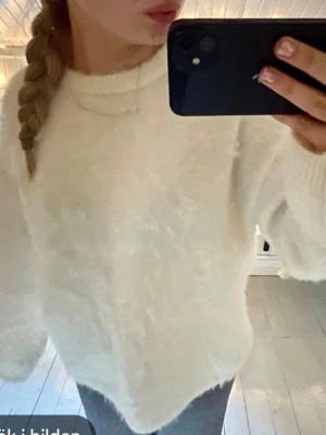 Vit fluffig mohair stickad tröja - Mysig vit stickad tröja med fluffig textur och avslappnad passform. Tröjan har rund halsringning och långa ärmar med ribbade muddar. Perfekt för kalla dagar när du vill vara både bekväm och stilren.