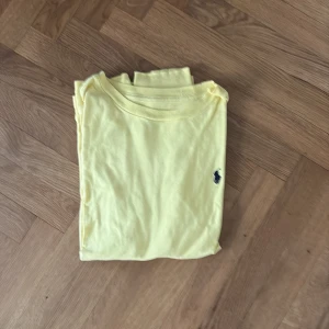 Gul långärmad t-shirt Polo Ralph Lauren - Fräsch gul långärmad t-shirt från Polo Ralph Lauren med klassisk rund hals och den ikoniska blå logon broderad på bröstet. Tillverkad i mjuk bomull som känns skön mot huden. Perfekt för dig som gillar stilrena och enkla plagg med en touch av lyx.