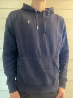Mörkblå hoodie från Polo Ralph Lauren - Mörkblå hoodie från Polo Ralph Lauren.     Tröjan är i fint skick med inga skador eller fläckar. Storlek M. Skriv om ni undrar något eller har några frågor!