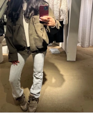 Olivgrön utility bomberjacka - Snygg olivgrön bomberjacka med stora fickor och dragkedja framtill. Jackan har en loose passform och långa ärmar, perfekt för lager på lager. Stilsäker och enkel att matcha till olika outfits.