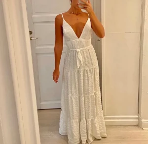 Vit långklänning med volanger - Superfin vit långklänning med smala axelband, djup v-ringning och knyt i midjan. Klänningen har volanger i flera lager och ett lätt, luftigt tyg som ger en romantisk känsla. Bilderna nedan är från den tidigare säljarens annons och används med deras tillåtelse. Produkten är i samma skick som på bilderna✨