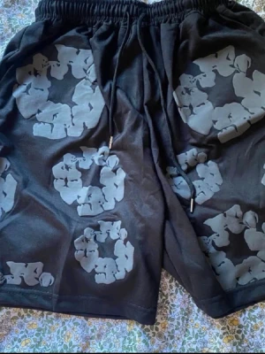 Svarta shorts med grått blommönster - Säljer ett par svarta shorts med grått blommönster i cirklar. Shortsen har resårmidja med snörning och en bakficka. Perfekta för sommaren och riktigt sköna att bära till vardags.