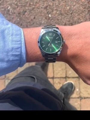 Grön klocka med metallarmband - Stilren klocka från Doventi med grön urtavla och datumvisning. Klockan har ett klassiskt silverfärgat metallarmband och boett i metall. Perfekt accessoar för dig som vill sticka ut med en unik färg på handleden.