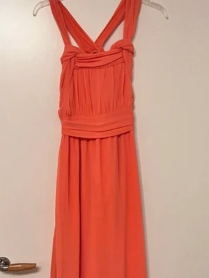 Lång korall klänning från Nelly - Snygg långklänning i stark orange färg med breda korsade axelband och markerad midja. Klänningen har ett elegant fall och plisserade detaljer upptill. Perfekt för dig som vill sticka ut med en färgstark look.
