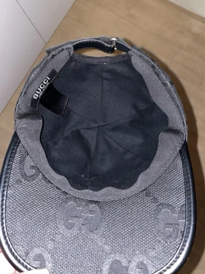 Svart keps från Gucci med GG-mönster - Snygg svart keps från Gucci med det klassiska GG-monogrammet över hela kepsen. Kepsen har böjd skärm med svart kant i läderlook och justerbar rem bak. Tillverkad i slitstarkt tyg med exklusiv känsla och diskret logga på insidan.