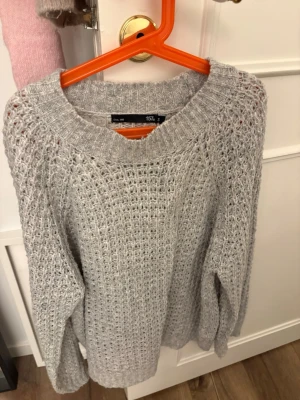 Ljusgrå stickad tröja från 157 - Ljusgrå stickad tröja från 157 med grovstickad struktur och bred ribbad halsringning. Tröjan har avslappnad passform och långa ärmar, perfekt för lager på lager. Materialet känns mjukt och mysigt, idealiskt för kyligare dagar.