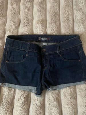 Mörkblå jeansshorts Zara - Snygga mörkblå jeansshorts från Zara med klassisk femficksdesign och uppvikta benslut. Shortsen har normal passform, bälteshällor och kontrastsömmar. Perfekta för varma dagar och enkel att matcha med olika toppar.