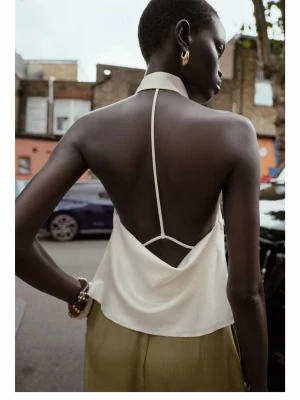 Vit prickig halterneck topp - Snygg vit halterneck topp med öppen rygg och smala band. Materialet har subtila prickar och glitter som ger en extra touch. Perfekt för dig som gillar trendiga och unika plagg med cool design.