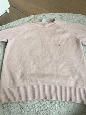 Ljusrosa stickad tröja - Mysig ljusrosa stickad tröja med rund halsringning och ribbade muddar vid ärmslut och nederkant. Tröjan har en enkel och stilren design, perfekt för lager på lager och passar till det mesta. Materialet känns mjukt och behagligt mot huden.