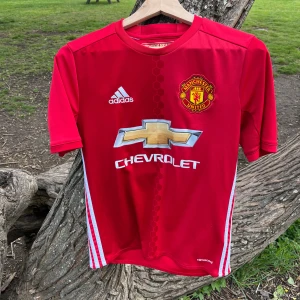 Manchester United Hemmatröja 2016/2017 #9 Ibrahimovic - Röd Manchester United fotbollströja från Adidas med tryck av Ibrahimovic och nummer 9 på ryggen. Tröjan har korta ärmar, vita detaljer på sidorna och klubbmärke samt sponsorlogga på bröstet. Perfekt för fans av Zlatan och United.