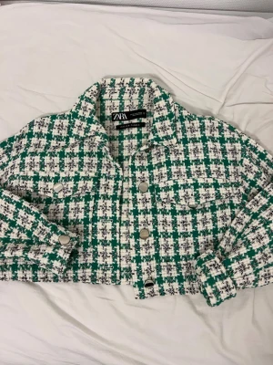 Grön och vit rutig kavaj från Zara - Trendig kavaj från Zara i grön och vit rutigt mönster, tillverkad av italienskt tyg. Kavajen har silvriga knappar framtill och på ärmarna samt två bröstfickor. Perfekt för dig som vill sticka ut med en cool och modern look.