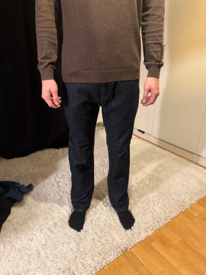Mörkblå raka jeans herr - Säljer ett par mörkblå jeans med rak passform. Klassisk femficksmodell och normal midja. Jeansen har en stilren look och är tillverkade i denim. Perfekta för dig som gillar en enkel och tidlös stil.