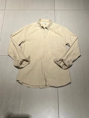 Beige skjorta, Filippa K - Klassisk beige skjorta i bomull med lång ärm, bröstficka och knappar framtill. Skjortan har en enkel, avslappnad passform och en stilren krage. Perfekt för dig som gillar en clean och tidlös look.