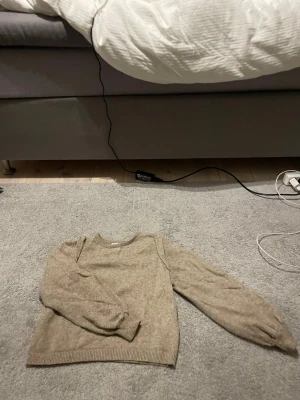 Beige stickad tröja - Mysig beige stickad tröja med rund hals och långa ärmar. Tröjan har ribbade muddar vid ärmslut och nederkant, vilket ger en klassisk och enkel look. Har puffiga armar och har blivit sydd då de var ett litet hål men de syns inte att de har blivit sydd. Är i storlek S men är mer som XS.