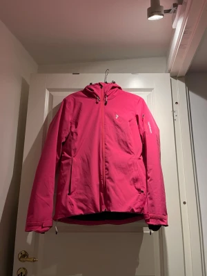 Rosa skidjacka från Peak Performance - Snygg rosa skidjacka från Peak Performance med huva och dragkedja framtill. Jackan har två sidofickor med dragkedja och justerbar nederkant.