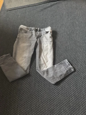 Grå jeans från Smog Denim 30/30 - Säljer ett par grå jeans från Smog Denim i storlek 30/30. Klassisk femficksmodell med dragkedja och knapp. Jeansen har en snygg tvättad look och raka ben. Perfekta för dig som gillar en avslappnad stil.