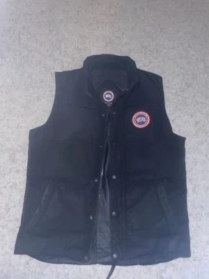 Svart dunväst från Canada Goose - Snygg svart dunväst från Canada Goose med klassisk logotyp på bröstet. Haft den ett tag nu och dags att sälja. Säljer för 1,6 köpt för runt 2,5 för länge sen. Men kom med bud !! Storlek S och sitter perfekt!