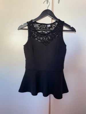 Svart topp - Snygg svart topp med spetsdetaljer upptill och i ryggen. Ärmlös modell med rund halsringning och figurnära passform upptill. Perfekt att styla med jeans eller kjol för en trendig look.