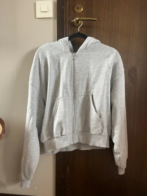 Grå zip hoodie med huva - En stilren grå hoodie med dragkedja framtill och två stora fickor från Hm. Hoodien har en klassisk huva och ribbade muddar vid ärmar och nederkant. Tillverkad i mjukt sweatshirtmaterial. Säljer för att den är för liten. Storlek S.