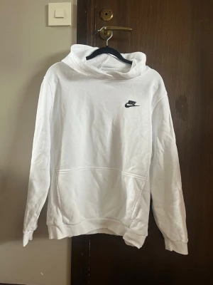 Vit hoodie från Nike med logga - Snygg vit hoodie från Nike med klassisk svart logga broderad på bröstet. Hoodien har en stor känguruficka framtill och en skön huva. Säljer för att den är för liten. Storlek 158-170cm.