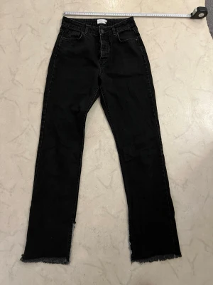 Svarta raka jeans från NA-KD Hanna Schönberg - Säljer ett par svarta raka jeans från NA-KD x Hanna Schönberg. Jeansen har hög midja, råa kanter vid bensluten och klassisk femficksdesign. Tillverkade i ett kraftigt denimtyg som ger en snygg vintagekänsla.
