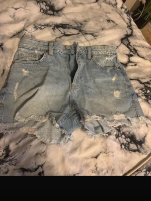 Shorts - Säljer ett par ljusblå jeansshorts från FB Sister i storlek S passar M Shortsen har fransig kant, slitna detaljer och klassisk femficksmodell. Perfekta för varma dagar och ger en avslappnad look.