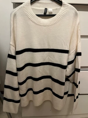Vit stickad tröja med svarta ränder - Säljer en vit stickad tröja från hm  med breda svarta horisontella ränder. Tröjan har rund halsringning, långa ärmar och ribbade muddar vid ärmslut och nederkant. Perfekt för dig som gillar en avslappnad och trendig look.