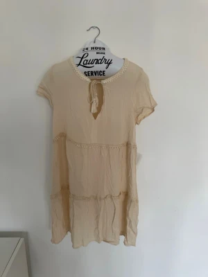 H&M - Beige klänning med knyt - Beige kortklänning med korta ärmar och dekorativ knytning vid halsen. 