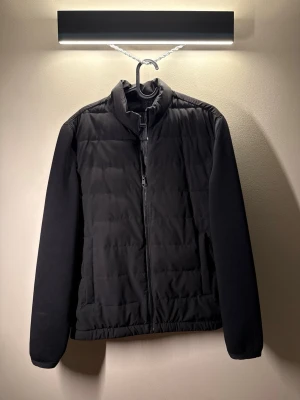 Svart pufferjacka från Zara - Snygg svart pufferjacka från Zara med quiltad front och släta ärmar. Jackan har dragkedja framtill, ståkrage och diskreta sidofickor. Materialet är lätt och ger en clean look, perfekt för kalla vinterdagar.