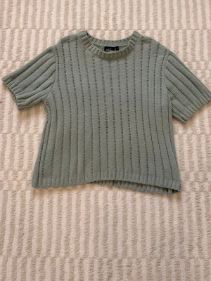 Grön ribbstickad topp från KappAhl - Kortärmad ribbstickad tröja i ljusgrönt från KappAhl. Tröjan har rund halsringning och ett luftigt, rakt snitt med vertikala hålstickade ränder. Storlek S, men passar även mig som brukar ha M